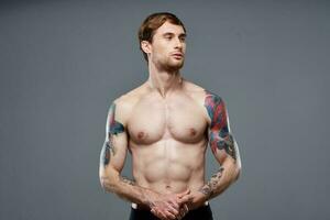 sportief Mens met tatoeages Aan zijn armen gemotiveerd omhoog druk op macho grijs achtergrond foto