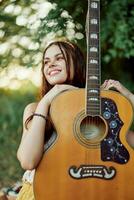 jong hippie vrouw met eco beeld glimlachen en op zoek in de camera met gitaar in hand- in natuur Aan een reis foto