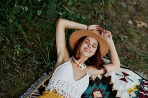 een vrouw in milieuvriendelijk kleding in een hippie kijken is aan het liegen Aan een gekleurde plaid glimlachen en op zoek Bij een herfst zonsondergang in natuur in de park. levensstijl Aan een reis van harmonie met de wereld foto