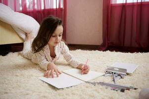 gelukkig weinig kind meisje in elegant pyjama met kleurrijk stippen, tekening afbeeldingen in albumkinderen hobby onderwijs foto