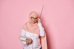 Arabisch moslim zwanger vrouw in roze hijaab, benadrukt school- leraar looks Bij camera door bril geïsoleerd Aan roze foto