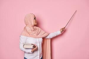 zelfverzekerd Arabisch moslim vrouw, school- leraar richten Bij kopiëren ruimte Aan roze achtergrond met een wijzer, uitleggen les foto
