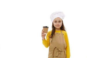 Kaukasisch kind meisje in chef-kok hoed en keuken schort, houdt meenemen drinken in beschikbaar papier beker. voedsel levering onderhoud foto