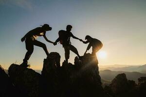 silhouet van samenspel van drie wandelaar helpen elk andere Aan top van berg beklimming team. samenspel vriendschap wandelen helpen elk andere vertrouwen bijstand silhouet in bergen, zonsopkomst. foto