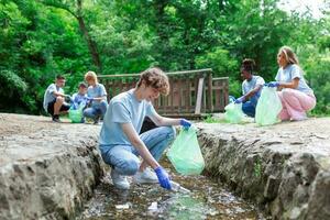 vrijwilliger jong Mens verzamelen plastic onzin Aan kust van de rivier. schoonmaak milieu concept foto