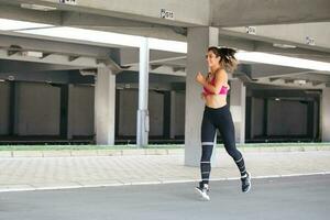 jong vrouw met fit lichaam jumping en rennen tegen grijs achtergrond. vrouw model- in sportkleding oefenen buitenshuis. foto