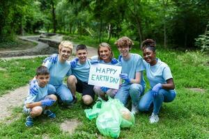 verschillend groep van mensen plukken omhoog uitschot in de park vrijwilliger gemeenschap onderhoud. gelukkig Internationale vrijwilligers Holding aanplakbiljet met 'Vrolijk aarde dag' bericht. foto