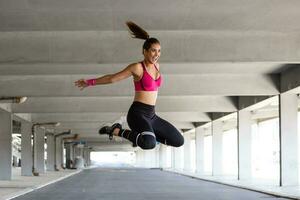 geschiktheid vrouw jumping buitenshuis in stedelijk omgeving. actief vrouw wezen vol van energie, springt hoog in lucht, bereidt zich voor voor sport wedstrijden. . gymnastiek concept foto