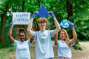 verschillend groep van mensen plukken omhoog uitschot in de park vrijwilliger gemeenschap onderhoud. gelukkig Internationale vrijwilligers Holding aanplakbiljet met 'Vrolijk aarde dag' bericht. foto