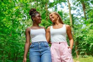 openhartig twee verschillend Dames wandelen samen buiten lachend en glimlachen foto