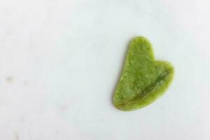 groen jade gua sha stimulator voor gezicht Aan wit marmer. foto