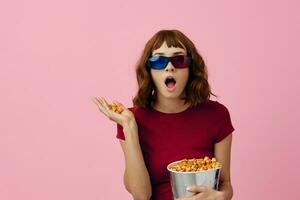 dolblij gelukkig schattig roodharige dame in rood t-shirt 3d bril met popcorn kijk maar film poseren geïsoleerd Aan over- roze studio achtergrond. kopiëren ruimte spandoek. mode bioscoop concept. vermaak aanbod foto