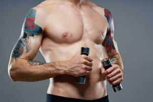 mannetje atleet met een tatoeëren Aan zijn arm naakt torso opgeblazen spieren halters geschiktheid foto