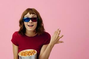 dolblij gelukkig schattig roodharige dame in rood t-shirt 3d bril met popcorn kijk maar film poseren geïsoleerd Aan over- roze studio achtergrond. kopiëren ruimte spandoek. mode bioscoop concept. vermaak aanbod foto