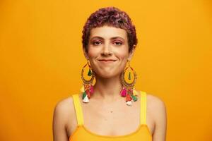 portret van een jong vrouw met een kort kapsel en gekleurde haar- glimlachen en tonen haar tong Bij de camera Aan een oranje achtergrond met oorbellen accessoires in de studio foto