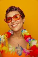 portret van een vrouw met een bloemen hawaiiaans krans in de omgeving van haar nek is hebben pret dansen en glimlachen in helder kleren Aan een oranje achtergrond vervelend zonnebril, levensstijl partij hawaiiaans stijl foto