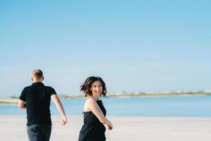jong stel een man met een meisje in zwarte kleren lopen op het witte zand
