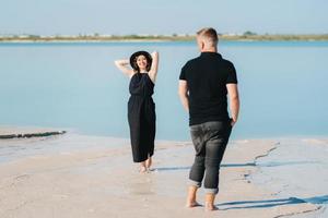 jong stel een man met een meisje in zwarte kleren lopen op het witte zand