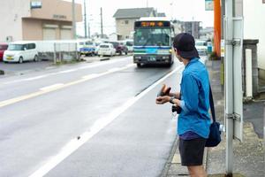 achterportret van niet-geïdentificeerde mannelijke toerist die op komende bus bij bushalte wacht. foto