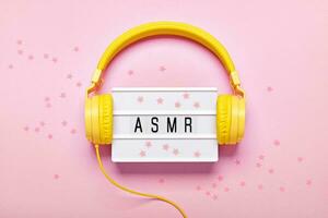 geel koptelefoon, asmr brieven lichtbak en confetti Aan roze achtergrond. asmr stress verlichtend geluiden concept, vlak leggen foto
