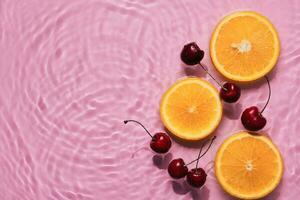 sinaasappels en kersen in roze water achtergrond met concentrisch cirkels en rimpelingen. verfrissend zomer concept, kopiëren ruimte foto