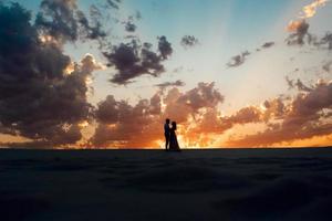 jong stel een man in zwarte rijbroek en een meisje in een roze jurk lopen langs het witte zand foto