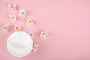 crème en bloemen op roze achtergrond, schoonheid huidverzorging cosmetica met kopie ruimte foto