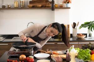 jonge vrouw die een hamburger in keuken met een glimlach en geluk kookt foto