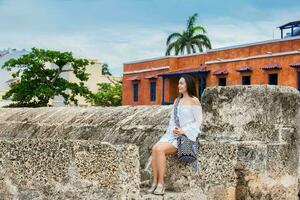 mooi vrouw Aan wit jurk zittend alleen Bij de muren omgeving de koloniaal stad van Cartagena de india's foto