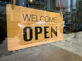 Welkom wij zijn Open alstublieft komen in teken Aan de glas deur van de koffie winkel foto