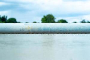 selectieve focus op regendruppels die onder een stalen balk hangen. close-up van waterdruppels onder metalen hek met onscherpe natuurlijke achtergrond foto