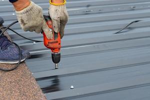 werknemers die een metalen dakplaat installeren met een elektrische boormachine. selectieve focus op het boorgereedschap tijdens het bouwen van het dak foto