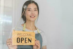 eigenaar bedrijf kleinhandel, aantrekkelijk Aziatisch jong vrouw hand- in draaien teken bord naar Open koffie winkel, heropenen op te slaan na dichtbij vergrendeling quarantaine in covid19. foto