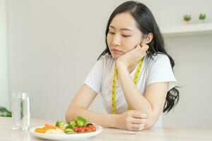 eetpatroon in verveeld gezicht, ongelukkig mooi Aziatisch jong vrouw Aan diëten, op zoek Bij salade bord Aan tafel, afkeer of moe met eten vers groenten. voedingsdeskundige van gezond, voeding van gewicht verlies. foto