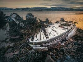 oud roestig visvangst boot verlaten door een storm Aan de winter oever. begraafplaats van schepen. foto
