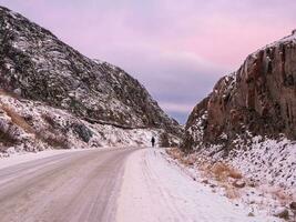 een besneeuwd weg uitrekken weg in de afstand tussen de heuvels. de magisch Purper kleur van ochtendgloren. foto