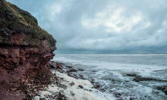 een rots klif bovenstaand de water met een getij kustlijn. wit zee. foto