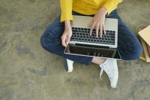 jong vrouw werken of aan het studeren online gebruik makend van laptop zittend Aan de vloer. foto