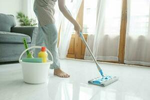 jong vrouw schoonmaak verdieping gebruik makend van dweilen Bij huis. foto