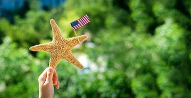 zeester houdt de Amerikaans vlag Aan een wazig groen achtergrond. arbeid dag vakantie concept. 4e van juli Verenigde Staten van Amerika onafhankelijkheid dag. kopiëren ruimte voor tekst. foto