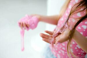 een weinig meisje gebrandschilderd haar haar- met slijm. kind haar- verstrikt in roze slijm. foto