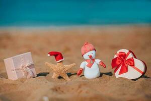 geschenk dozen, een zeester in een de kerstman hoed en een handgemaakt sneeuwman Aan de strand. vakantie Kerstmis concept. foto