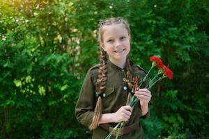 een meisje in een speciaal uniform met een st. George lint houdt drie anjers in haar handen. vakantie zege dag mei 9e. foto