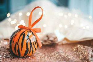 Kerstmis bal geschilderd net zo tijger strepen spins Aan wazig Kerstmis guirlande. achtergrond. 2022 is een jaar van de tijger. gelukkig nieuw jaar . symbool van jaar maan- Chinese kalender tijger Aan Kerstmis bal . foto