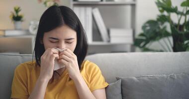 Aziatisch jong vrouw koorts niezen in blazen haar neus- in papier zakdoek Bij huis foto