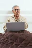 een senior Mens in zijn slaapkamer met laptop foto