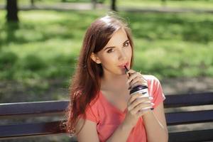 jonge vrouw nippend van een drankje in een park foto