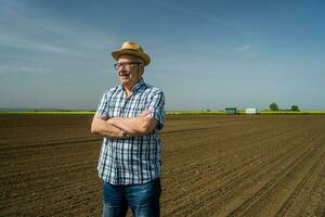 een senior boer staand in zijn eigen maïs veld- foto