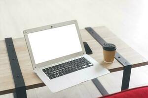 mockup laptop computer met blanco wit scherm Aan klein tafel met koffie papier beker. foto