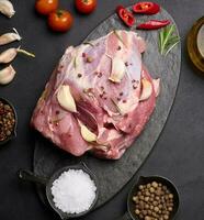 een stuk van varkensvlees ham Aan een zwart bord en specerijen olijf- olie, zout, rozemarijn Afdeling en peper foto